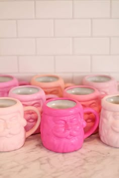 pink and white mugs with faces on them sitting on a marble counter in front of a brick wall