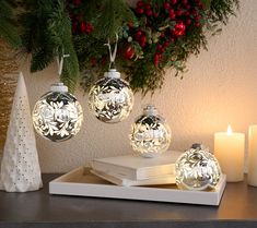 three christmas ornaments sitting on top of a table next to candles and a tree branch