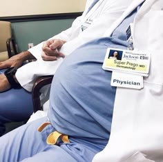 a man sitting in a chair with his back turned to the camera, wearing a white lab coat and blue pants