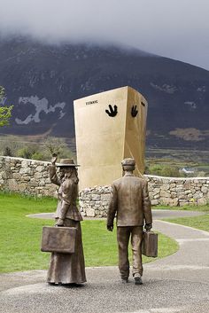 a statue of two people carrying boxes on their heads, walking down a path with a mountain in the background