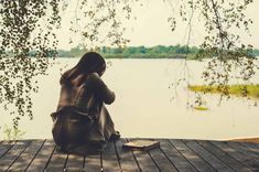 a woman sitting on a dock looking at the water