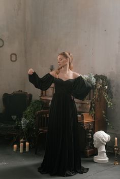 a woman standing in front of a piano wearing a black dress with long sleeves and an open shoulder