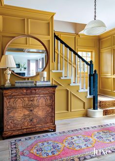 a living room with yellow walls and wooden furniture on the floor, along with a round mirror