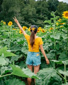 a woman standing in the middle of a sunflower field with her arms raised up