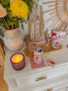 a white dresser topped with lots of clutter next to a vase filled with flowers