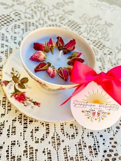 a teacup filled with flowers on top of a white doily next to a pink bow