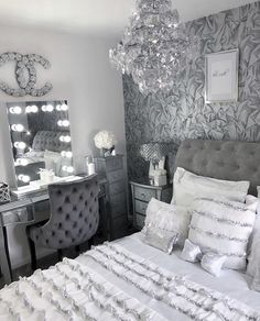 a white bed sitting next to a desk with a mirror above it and a chandelier hanging from the ceiling