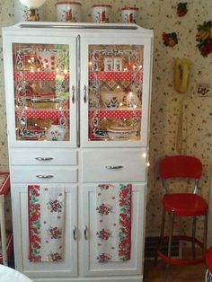 a white china cabinet with glass doors and red chairs next to it in a room