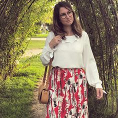 a woman wearing glasses and a white shirt is standing in front of some trees with her hand on her hip