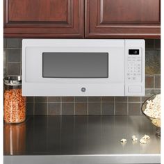 a white microwave oven sitting on top of a kitchen counter next to wooden cupboards