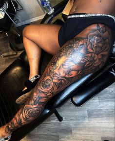 a woman is sitting in a chair with her leg covered by black and grey tattoos