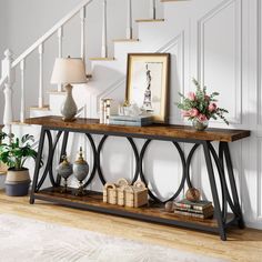 a console table with vases and flowers on it in front of a stair case