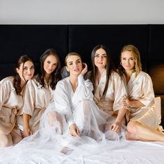 four women in robes are sitting on a bed and posing for the camera with their legs crossed