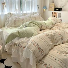 an unmade bed in a bedroom next to a window with white curtains and pillows