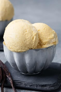 two scoops of vanilla ice cream in a metal bowl on top of a slate board