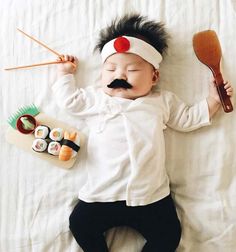 a baby laying on top of a bed with sushi and chopsticks