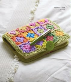 a crocheted book with a green button on the cover and a white bed sheet