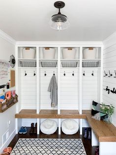 a mud room with white walls and baskets on the wall, two benches in front of them