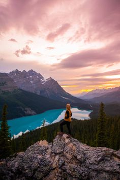 a woman sitting on top of a large rock next to a lake in the mountains