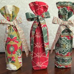 three wine bottle wrapped in fabric and tied with ribbon, sitting on a wooden table