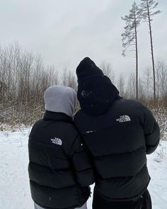 two people standing in the snow facing each other with their backs turned to the camera