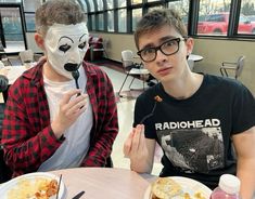 two young men sitting at a table with plates of food and masks on their faces