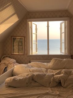 an unmade bed sitting in front of a window with the ocean out to sea