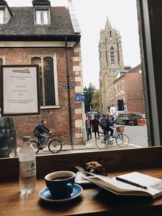 two people riding bikes on a street next to a building and a cup of coffee