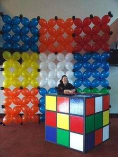 a woman standing behind a rubik cube in front of balloons on the wall,