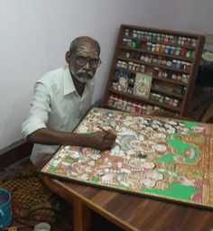 a man is sitting at a table with an elaborate painting on it in front of him