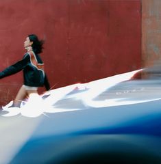 a woman walking down the street in front of a red wall