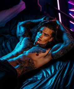 a man with tattoos laying on top of a bed in a room filled with neon lights