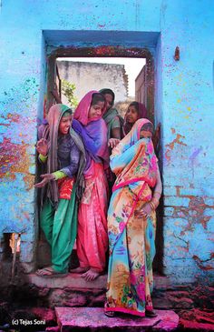 three women in colorful sari standing at the entrance to a blue building