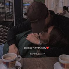 a man and woman kissing in front of two cups of coffee on a table with the caption you hug = my therapy