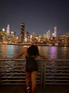 a woman standing on the edge of a pier looking at the city lights in the distance