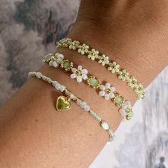 a woman's arm wearing three bracelets with flowers and heart charms on them