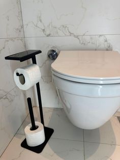 a white toilet sitting in a bathroom next to a roll of toilet paper on a black stand