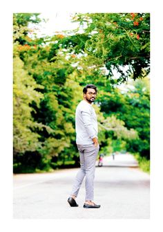 a man standing on the side of a road in front of some trees and bushes