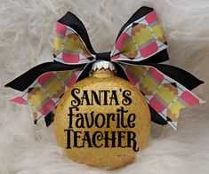 a yellow ornament with the words santa's favorite teacher on it and a bow