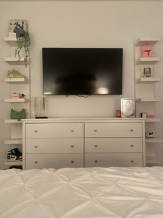 a flat screen tv mounted on the wall above a bed with white sheets and pillows