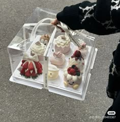 a person is holding a clear box filled with cupcakes and strawberries on display