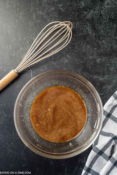 a glass bowl filled with brown liquid next to a whisk on a black counter