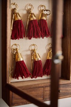 six red tasseled keychains hanging on a wooden frame in a display case