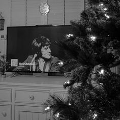 black and white photograph of woman on television screen next to christmas tree in kitchen area