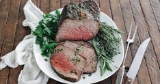 steak with herbs on a white plate next to knife and fork