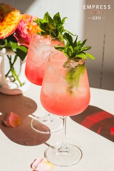 two glasses filled with pink lemonade and mint garnish sitting on a table