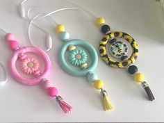 three necklaces with beads and tassels are on a white table next to a vase