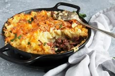 a casserole dish with meat and vegetables in it on a cloth next to a fork