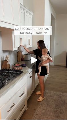 a woman holding a baby in her arms while standing next to a stove top oven