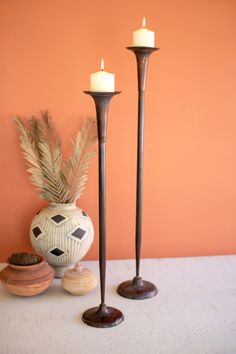 two candles sitting next to each other in front of a vase with a plant on it